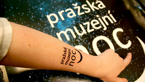 Za vyplnění zbavného kvízu děti obdrží nalepovací obtisk. Ruka s tetovacím obtiskem s logem Muzejní noci ukazující na plakát akce