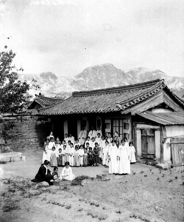 Americká misionářská škola v Koreji- skupina dívek a dětí s učiteli a misionářkami stojí před budovou. 1901 Fotografická pozůstalost E. St. Vráze