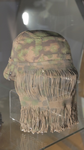 Fotografie. Přilba Waffen SS pro ostřelovače s maskovacím potahem a síťkou. Zdroj: Národní muzeum