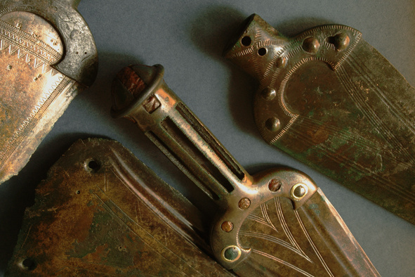 Fotografie. Depot bronzových dýk nalezený mezi obcemi Praha-Suchdol a Únětice, v pásu buližníkových skalek zvaných Kozí Hřbety, patří mezi nejvýznamnější středoevropské objevy starší doby bronzové. Lité bronzové předměty, uložené do země asi v 17. stol. př. n. l.,  jsou dekorovány precizní geometrickou rytou výzdobou, objeví se i jantarové a zlaté aplikace. Foto L. Káchová.