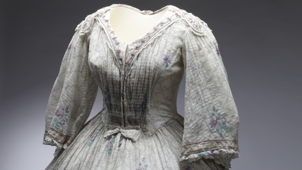 Šaty dámské bílé s drobným fialovým květinovým vzorem, tištěné jemné bavlněné plátno – mušelín, 1850–1860. Šaty pravděpodobně patřily principálce kočovné herecké společnosti Elišce Zöllnerové. Šaty dámské bílé s drobným fialovým květinovým vzorem, tištěné jemné bavlněné plátno – mušelín, 1850–1860. Šaty pravděpodobně patřily principálce kočovné herecké společnosti Elišce Zöllnerové.